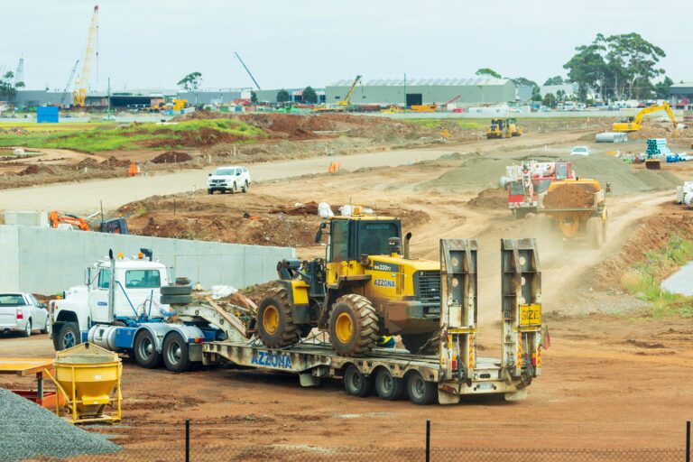 Lowboy trailer hauling a yellow wheel loader at a construction site