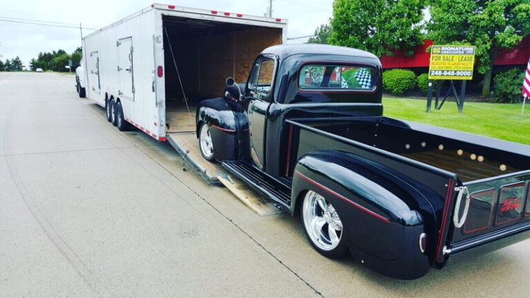 Black classic Ford pickup backing up the ramp into a white enclosed car trailer