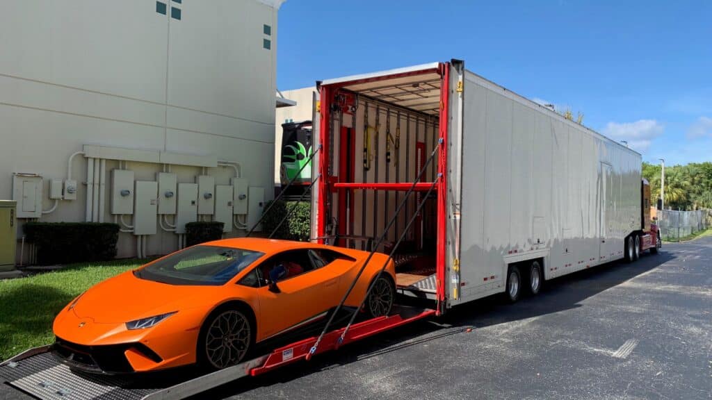 Orange sports car being loaded on a lift gate into an enclosed auto transport trailer