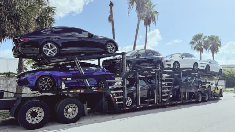 Two-level open car carrier loaded with cars under palm trees